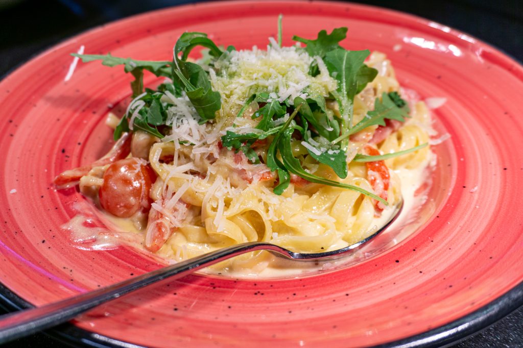 En alfredo pasta på en röd tallrik.