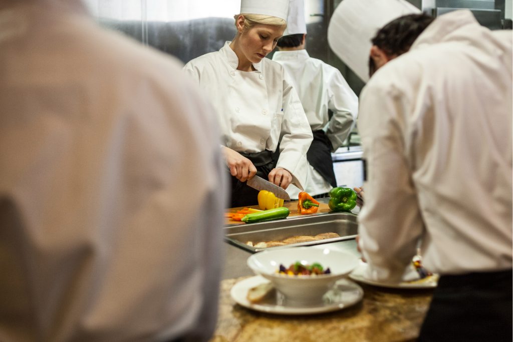Tre kockar förbereder mat och skär grönsaker.